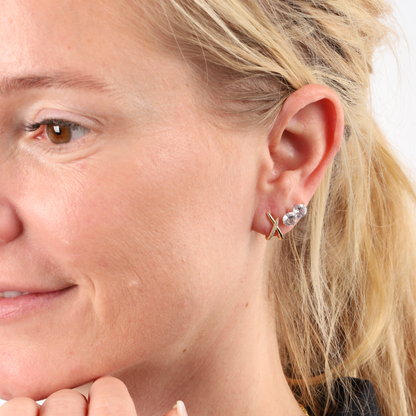 A woman wearing Mia Ishaaq® Gold Loop Cross Sparkle Stud Earrings smiles subtly.