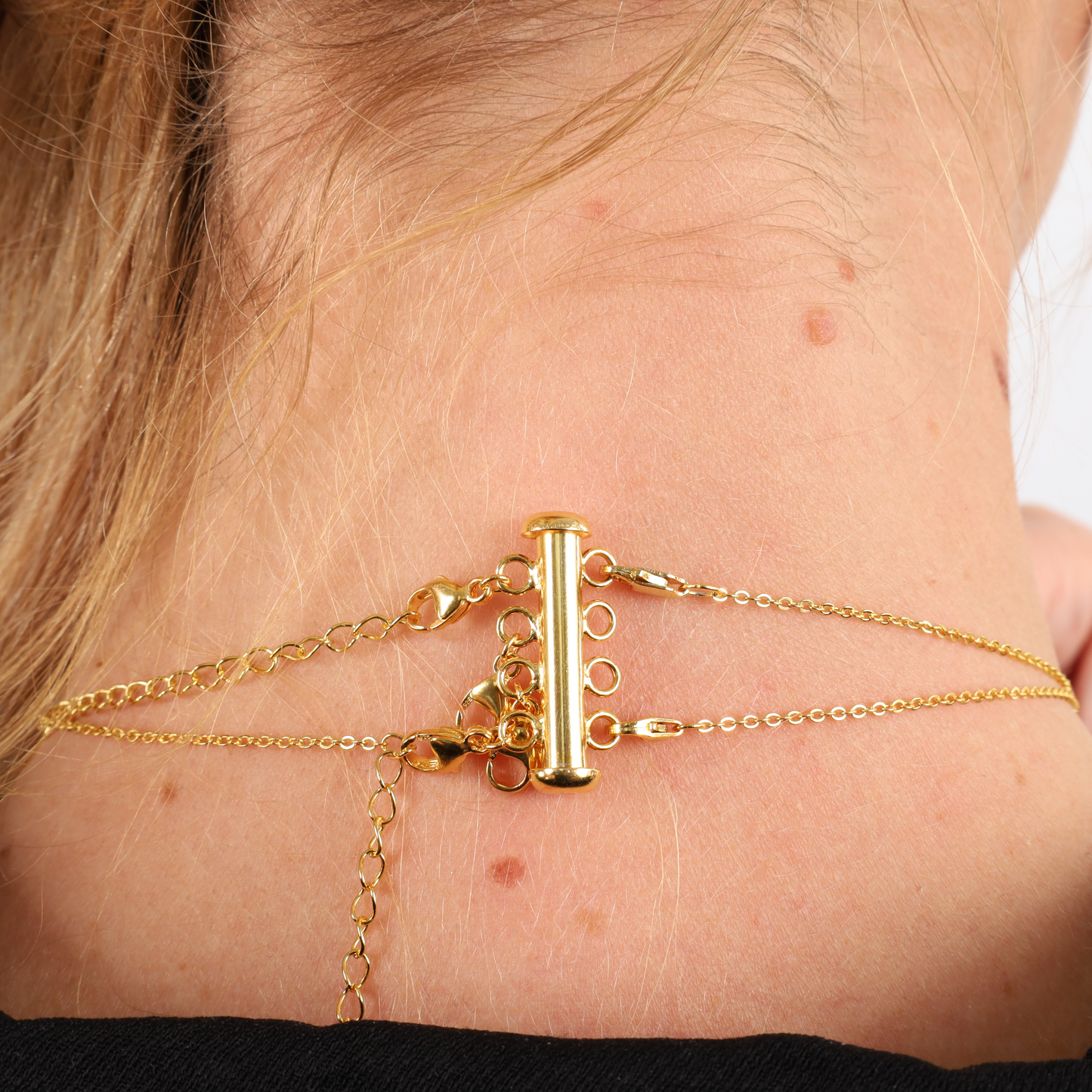 A close-up showcases the elegance and versatility of jewellery layering with Mia Ishaaq's Gold Necklace Layering Clip and chains on the back of a person's neck.