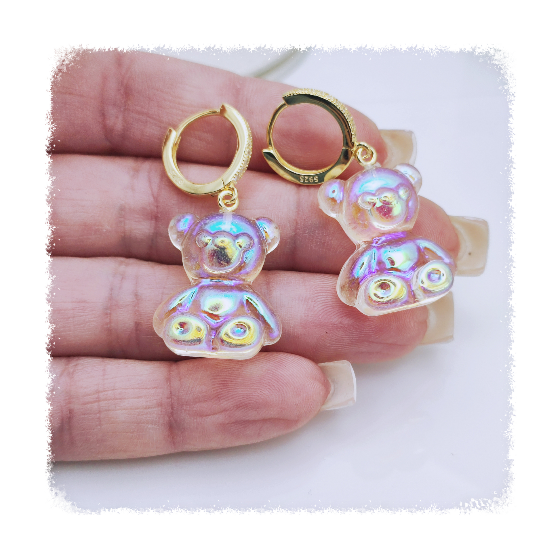 Mia Ishaaq's Shimmering Teddy Bear Earrings, featuring iridescent details and gold hoops crafted from 925 sterling silver, elegantly held in hands.